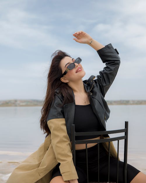 Brunette Woman in Jacket and Black Top Posing on Chair on Beach