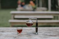 户外木桌上，特写镜头对准了虹吸咖啡机和咖啡杯