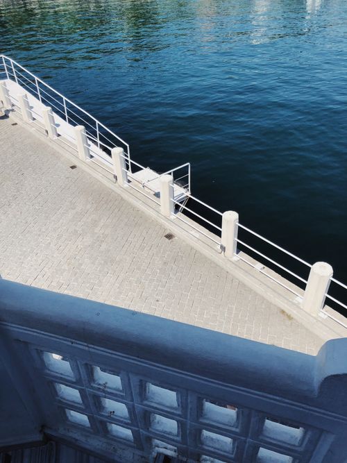 Free A high angle view of a sunlit urban pier with white railings by the water. Stock Photo
