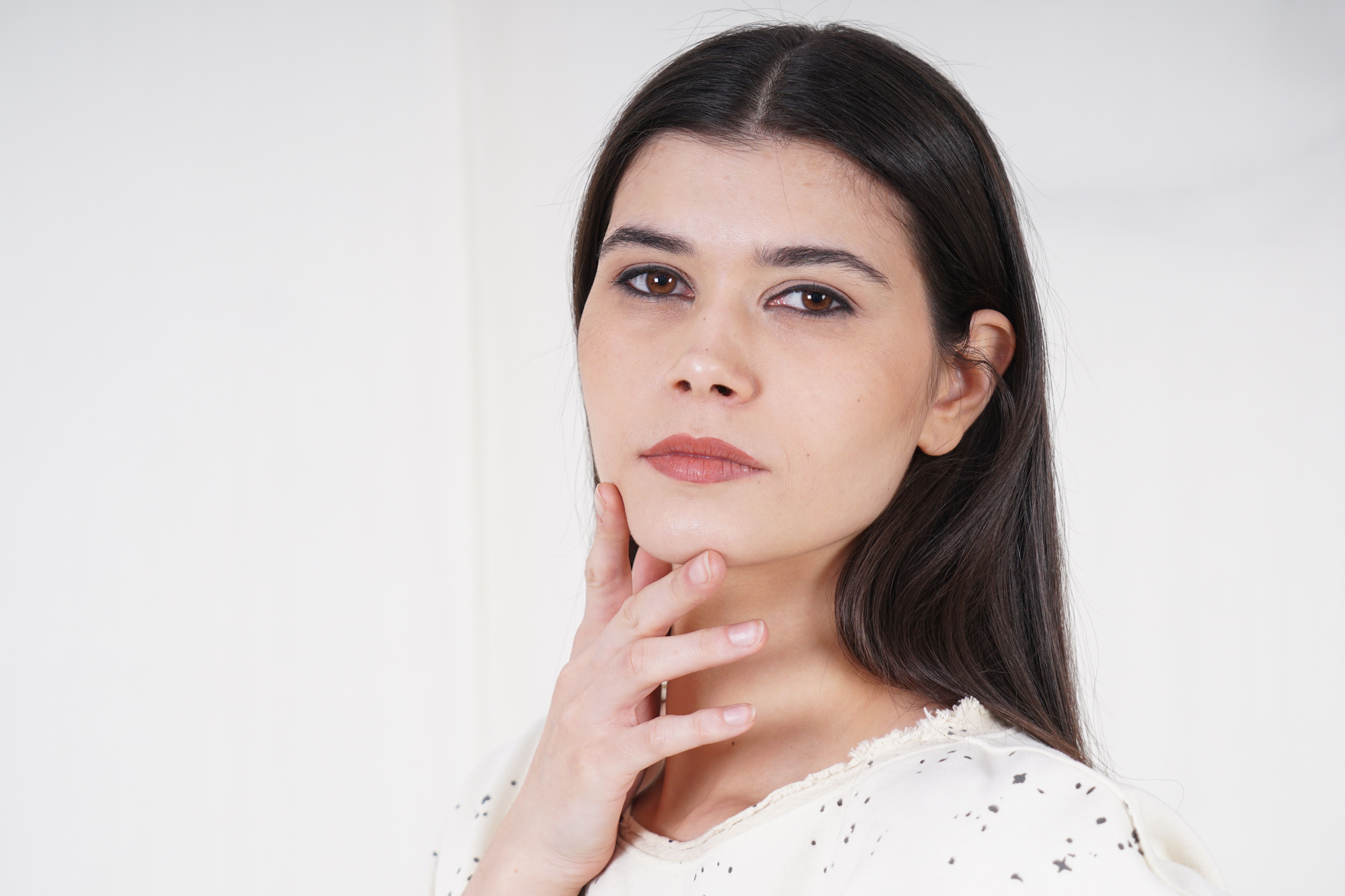 A serene studio portrait of a woman with long black hair against a white backdrop.