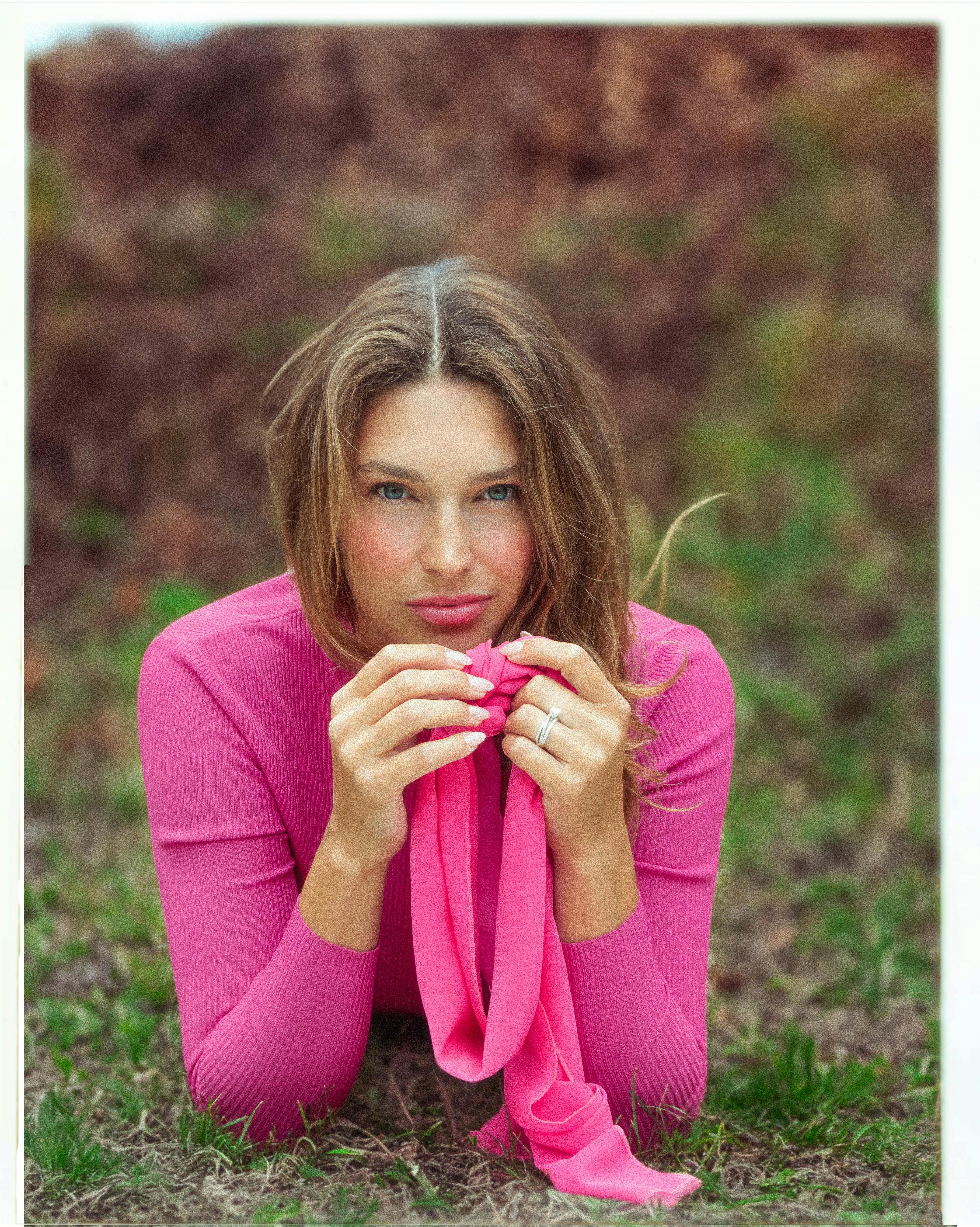 Portrait of a woman in a pink outfit lying on grass in Montreal park.