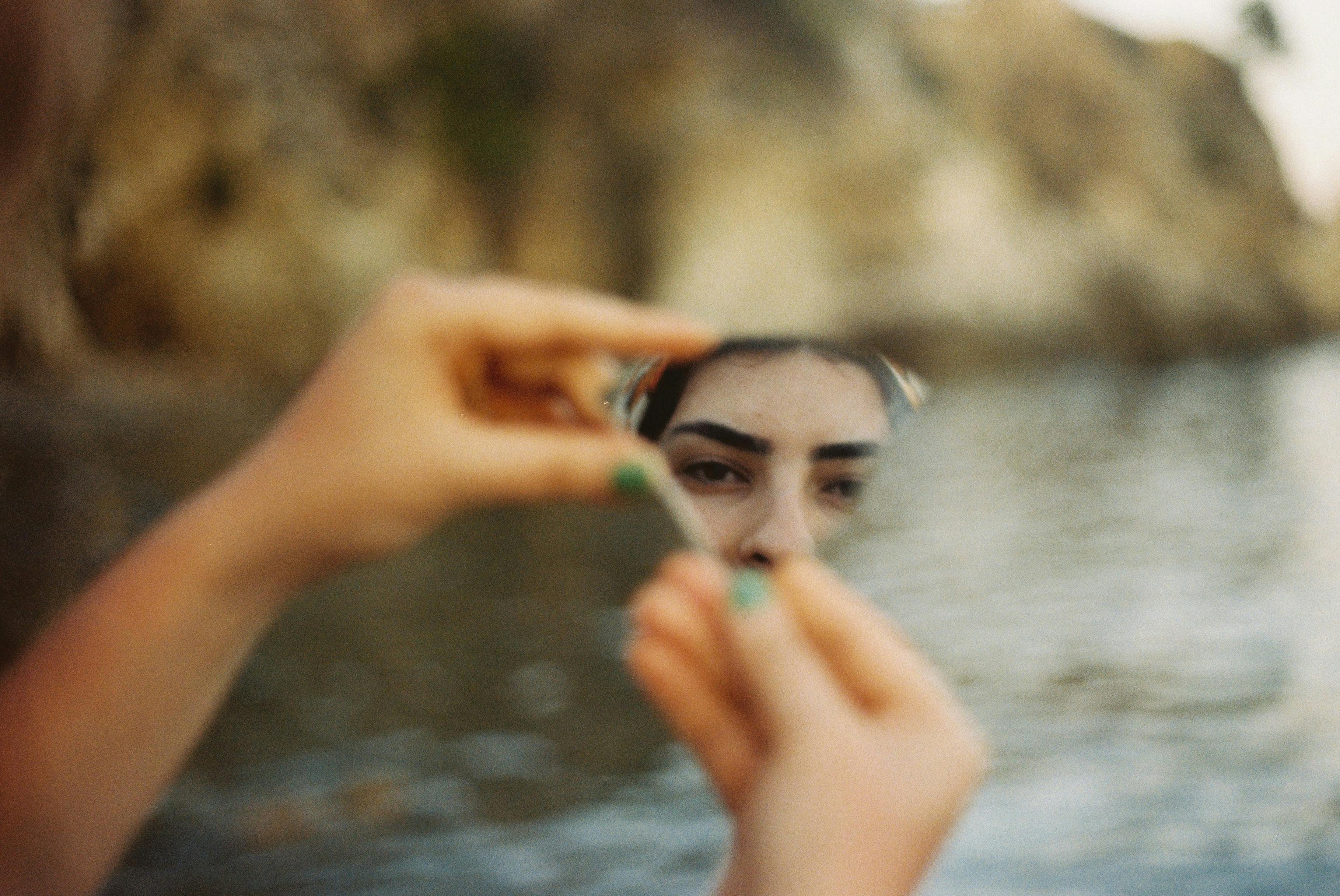 A person's face reflection in a mirror with a river background, creating a serene, introspective scene.