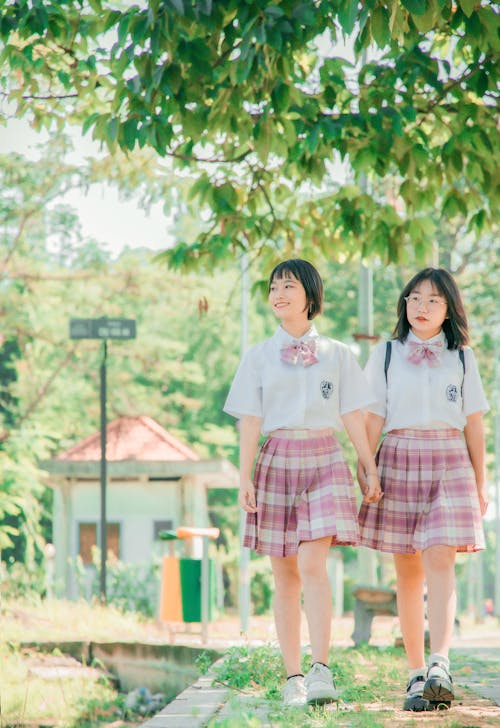 Women in Shirts and Skirts Walking under Tree Leaves