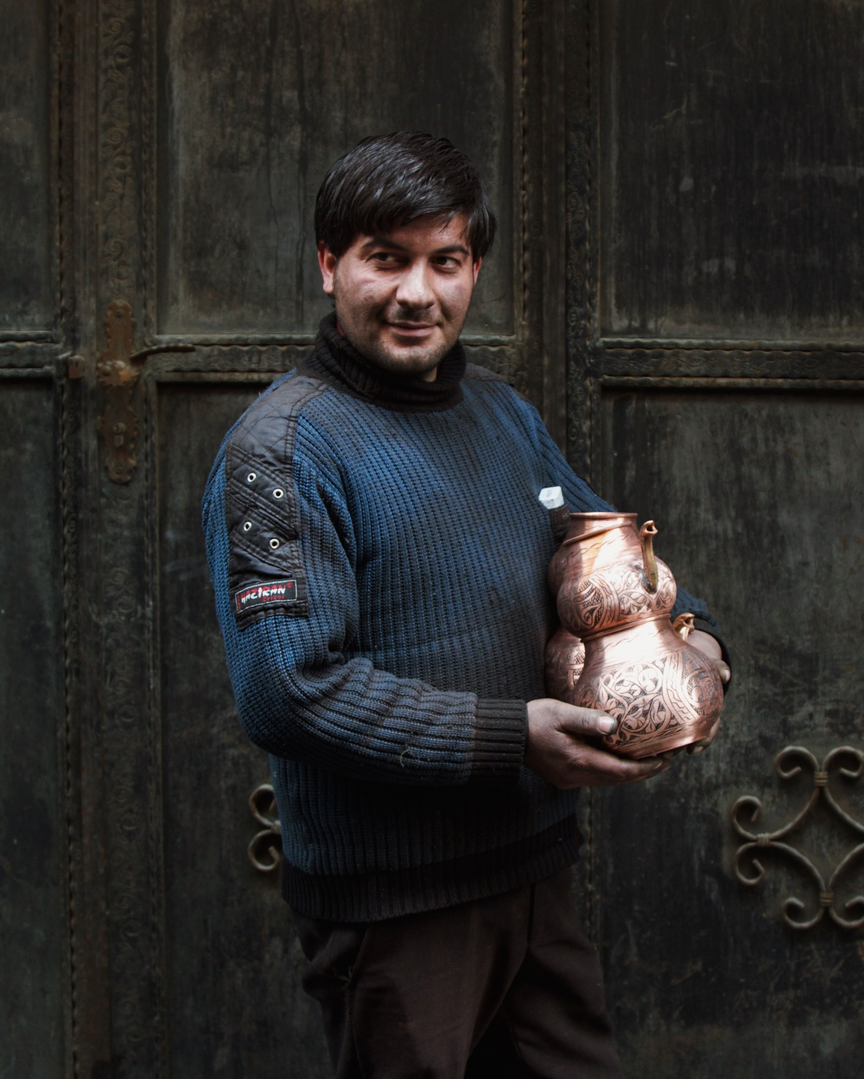Portrait of a man holding a traditional handmade bronze kettle indoors.