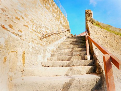 A scenic stone stairway with railings leading up under a bright blue sky.