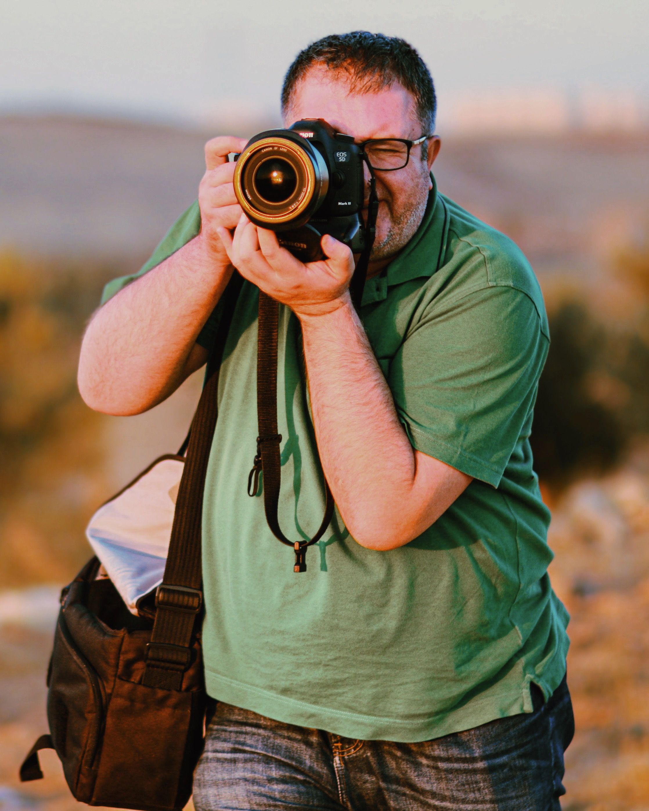 A man in a green shirt takes photos with a camera in a rural setting.
