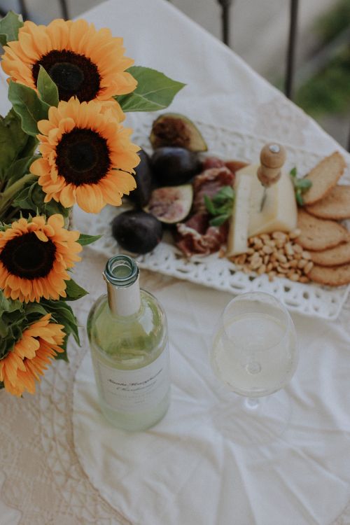Free A charming picnic setup with wine, cheese, and sunflowers on a table. Stock Photo