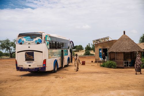 Free A white bus stops at a rural village with a tribal hut and local restaurant. Stock Photo