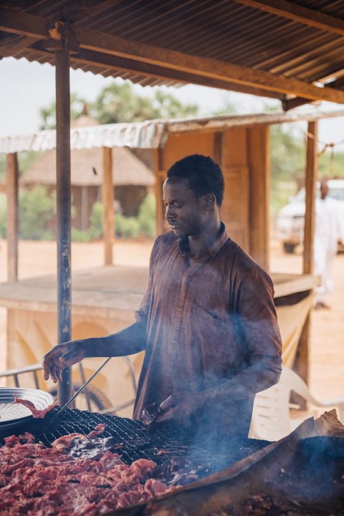 Free A man grilling meat outdoors, showcasing a smoky barbecue in a rural setting. Stock Photo