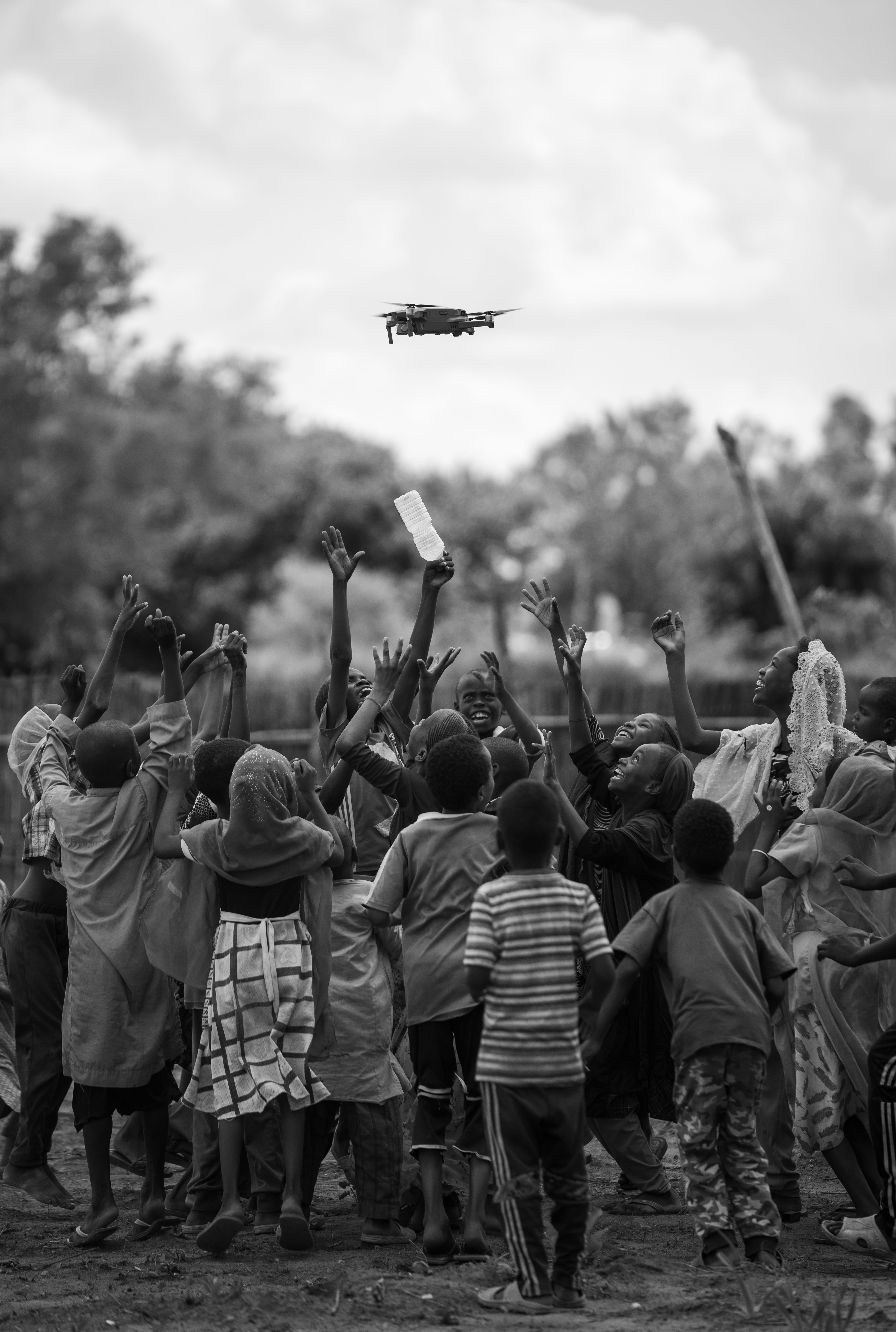A group of African children joyfully reaching towards a flying drone.
