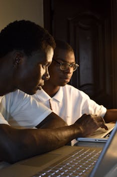 Two young professionals working intensely on laptops in a collaborative environment.