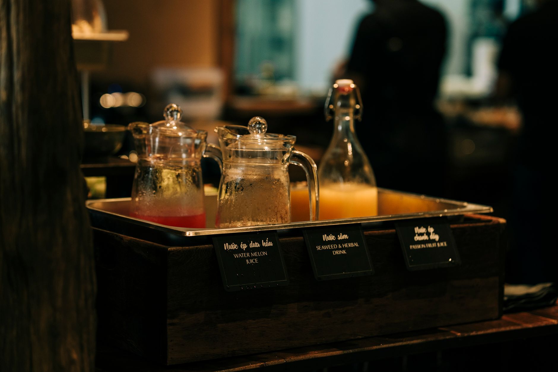 Various juices in glass jars displayed at a bar setting with dim lighting.