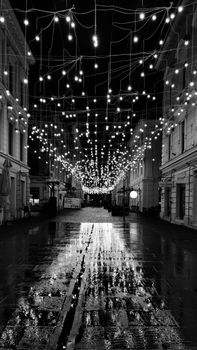 Black and white night photo of Timișoara street lit with strings of lights and wet pavement reflections.