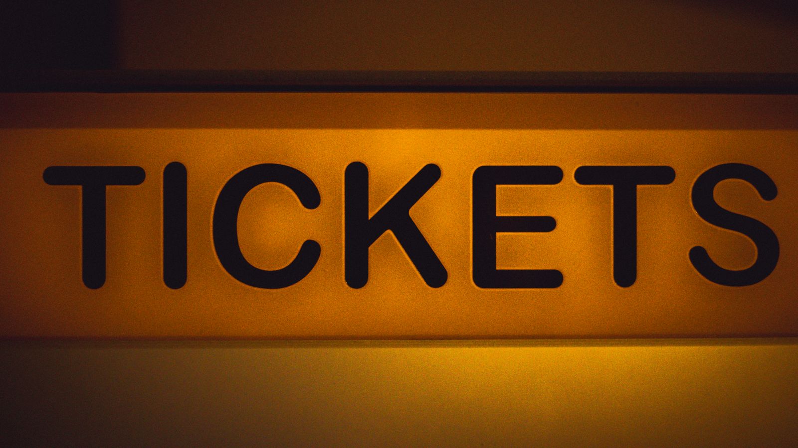Close-up of a glowing yellow TICKETS sign at a movie theater box office against a dark background, with no people in the frame, a real stock photo chosen because the story is about a worldwide box office record. It is not a still from either film