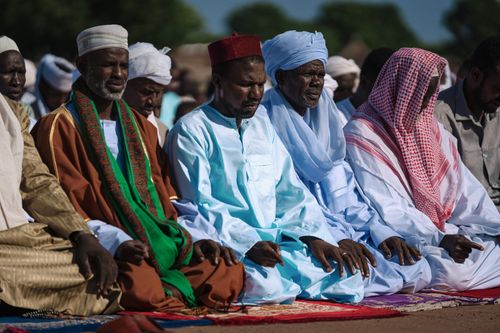 Free A group of men engaged in prayer outdoors, wearing traditional attire. Capturing cultural and religious practices. Stock Photo