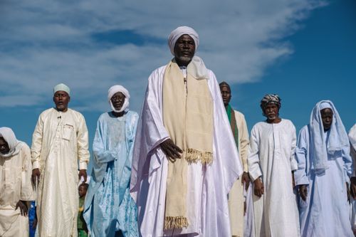 Free Group of men in traditional attire standing outdoors under a blue sky. Stock Photo