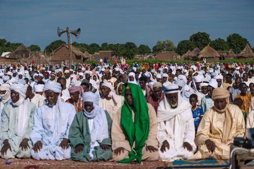 Free Hundreds of people kneeling in prayer in an open village setting, wearing traditional attire. Stock Photo