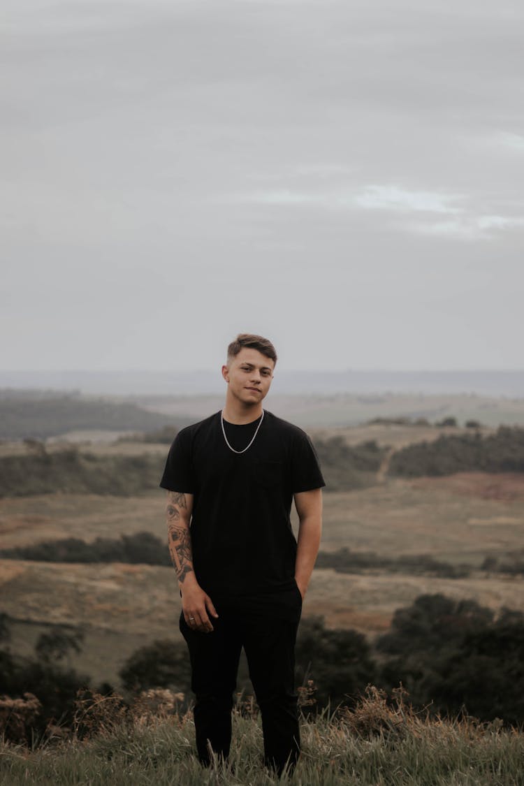 Young Man Wearing Black Clothes Standing On A Hill 