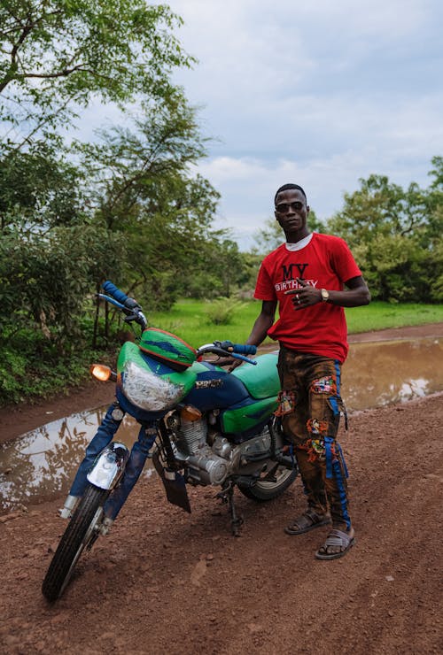 Man Standing by Motorcycle on Dirt Road