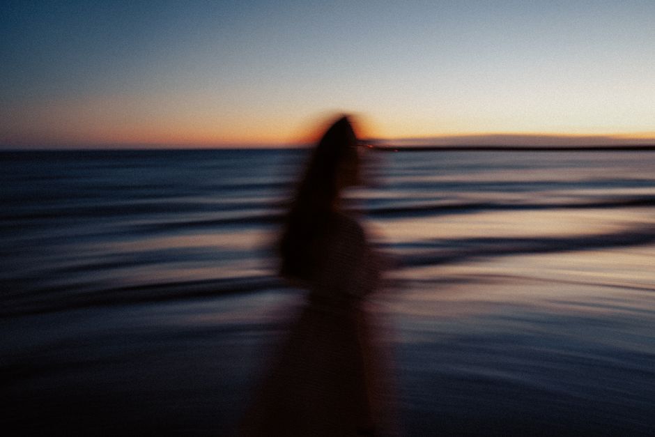 Artistic blurred silhouette of a woman walking along a serene seashore at sunset.