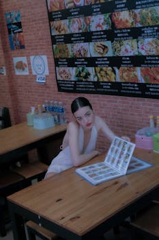 A fashionable woman in a white dress sitting at a Bangkok restaurant, browsing the menu.