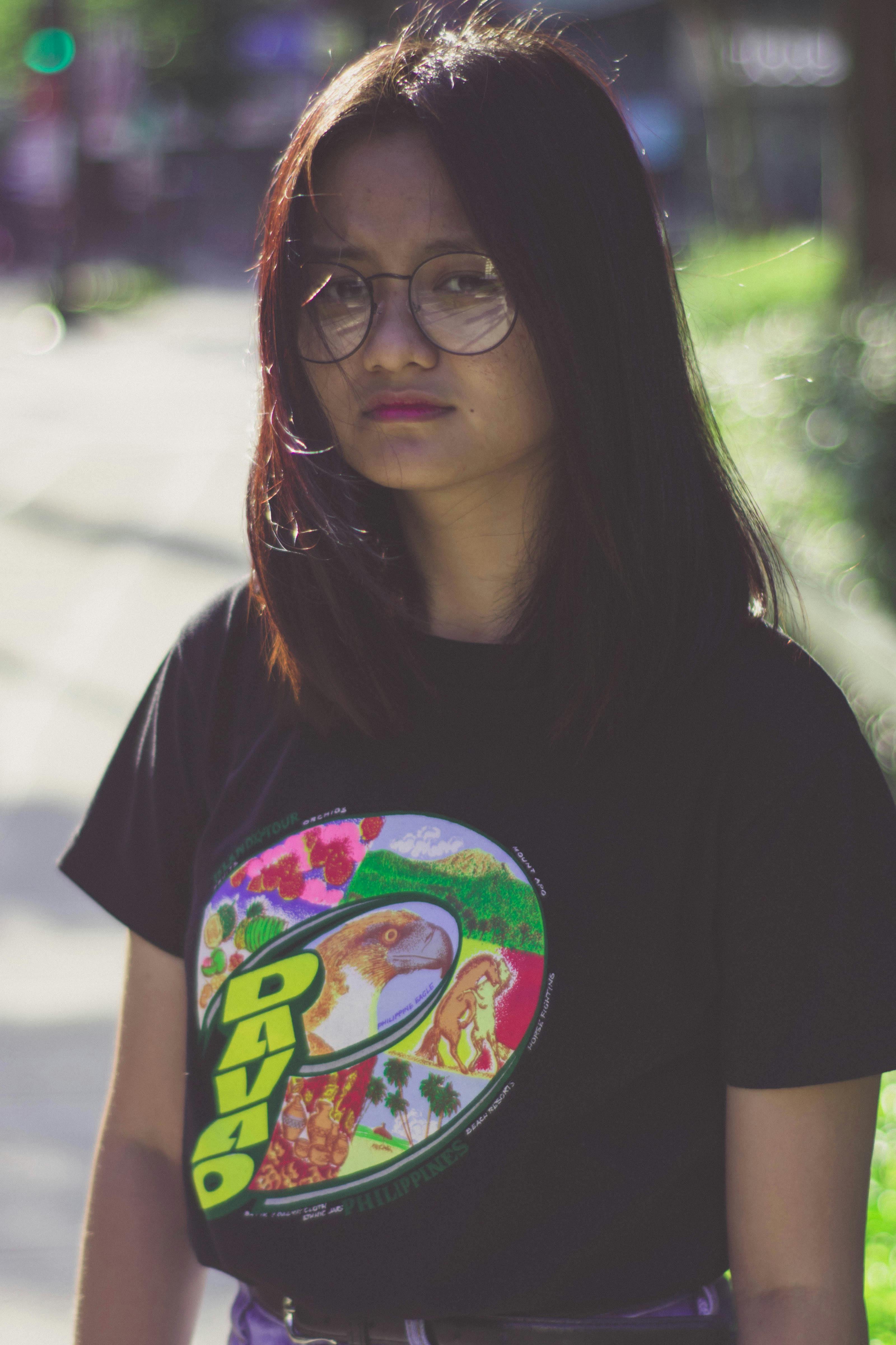 Portrait of a young woman wearing glasses and a graphic t-shirt, captured outdoors.