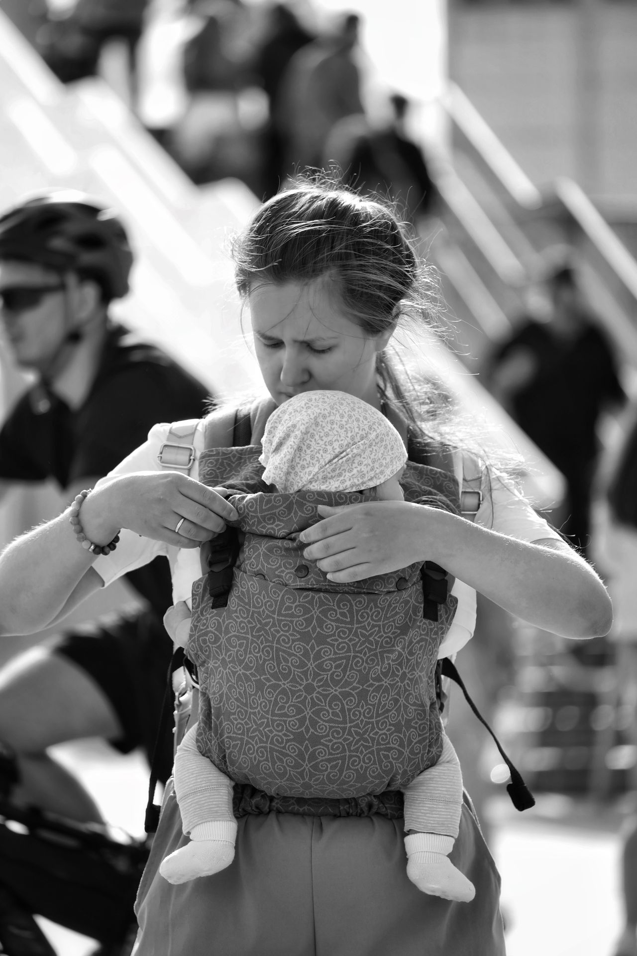 A woman carrying a baby in a front carrier with a bustling urban background.