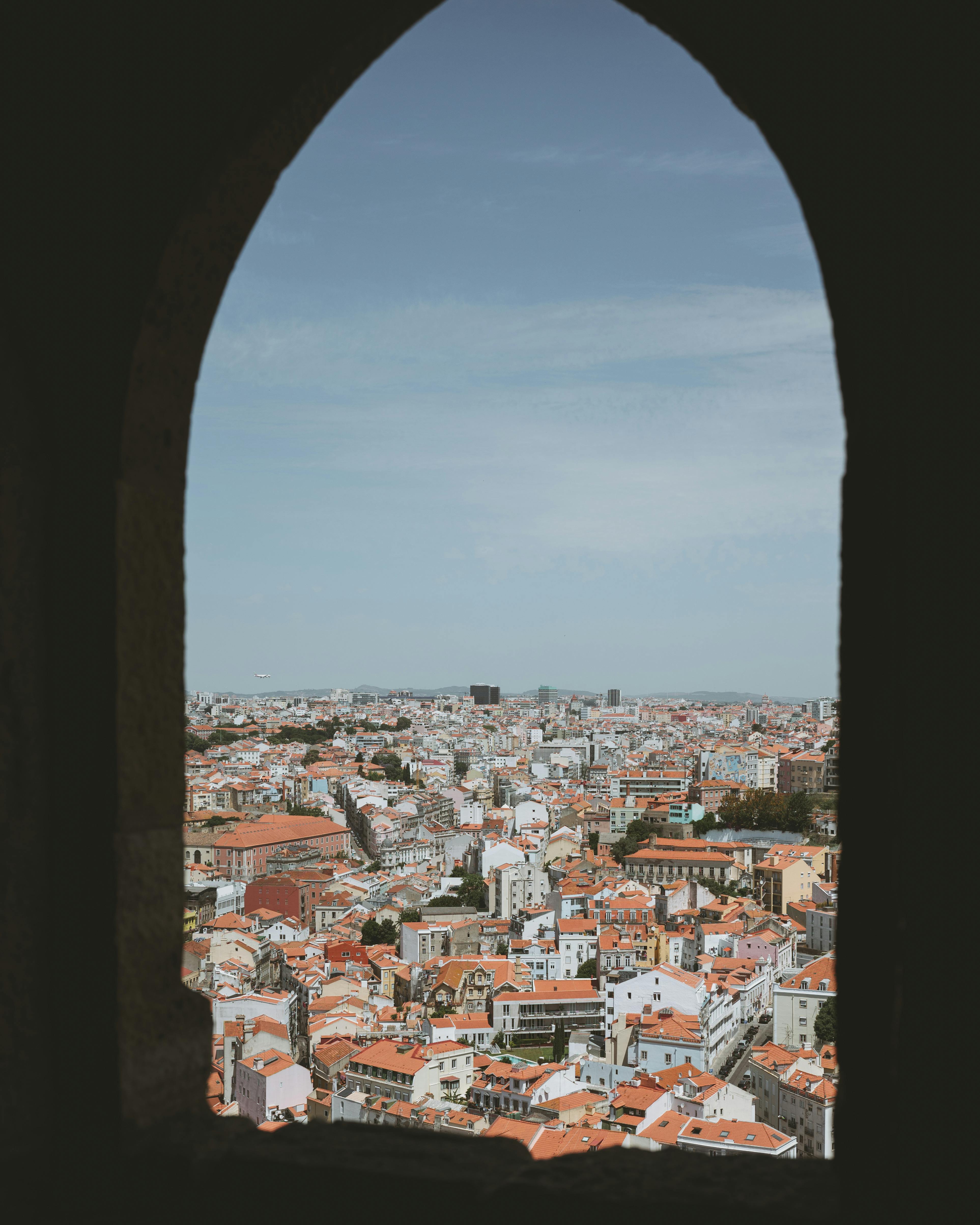 Discover the vibrant architecture of Lisbon through a classic arched window view, showcasing the city's skyline.
