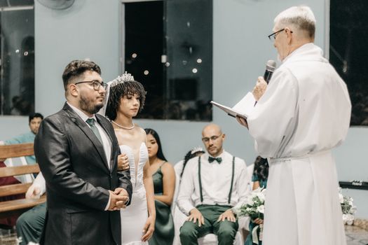 A traditional wedding ceremony indoors with a priest officiating the vows of a couple.