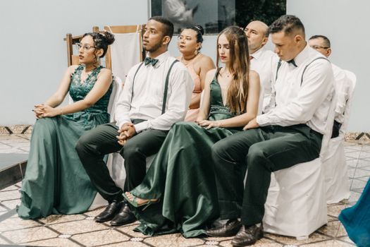 A group of elegantly dressed adults sitting attentively indoors at a wedding.