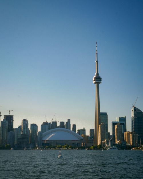 Free Breathtaking view of Toronto skyline featuring the iconic CN Tower at sunset with calm waters in the foreground. Stock Photo