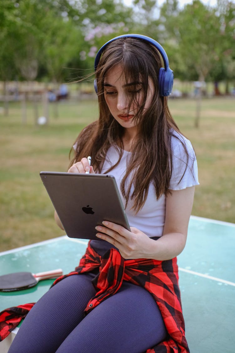 Brunette Woman With Tablet In Hand Sitting On Table In Park