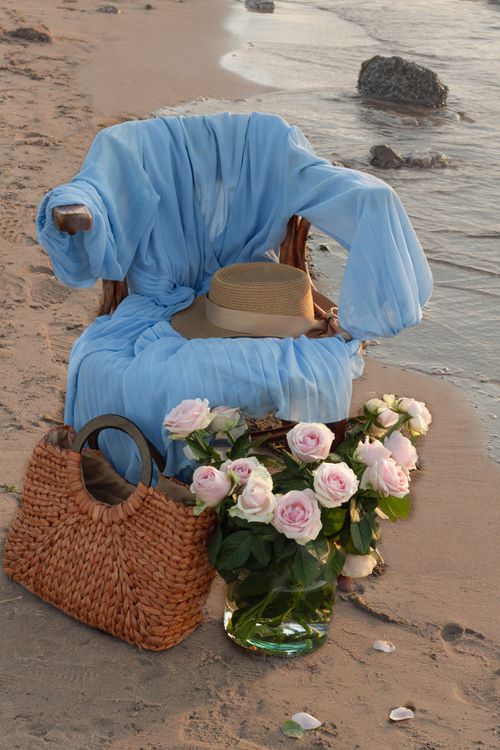 Free Elegant beachside chair draped in blue with a straw bag and pink roses. Stock Photo