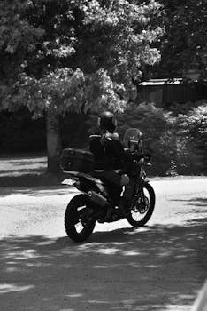Back view of a person riding a motorcycle on a dirt road surrounded by trees.