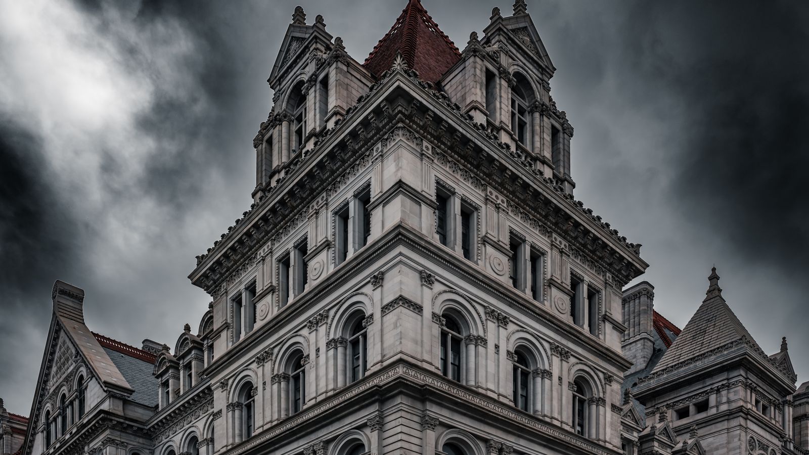 Dramatic view of the New York State Capitol building's Neo-Renaissance facade under stormy skies.
