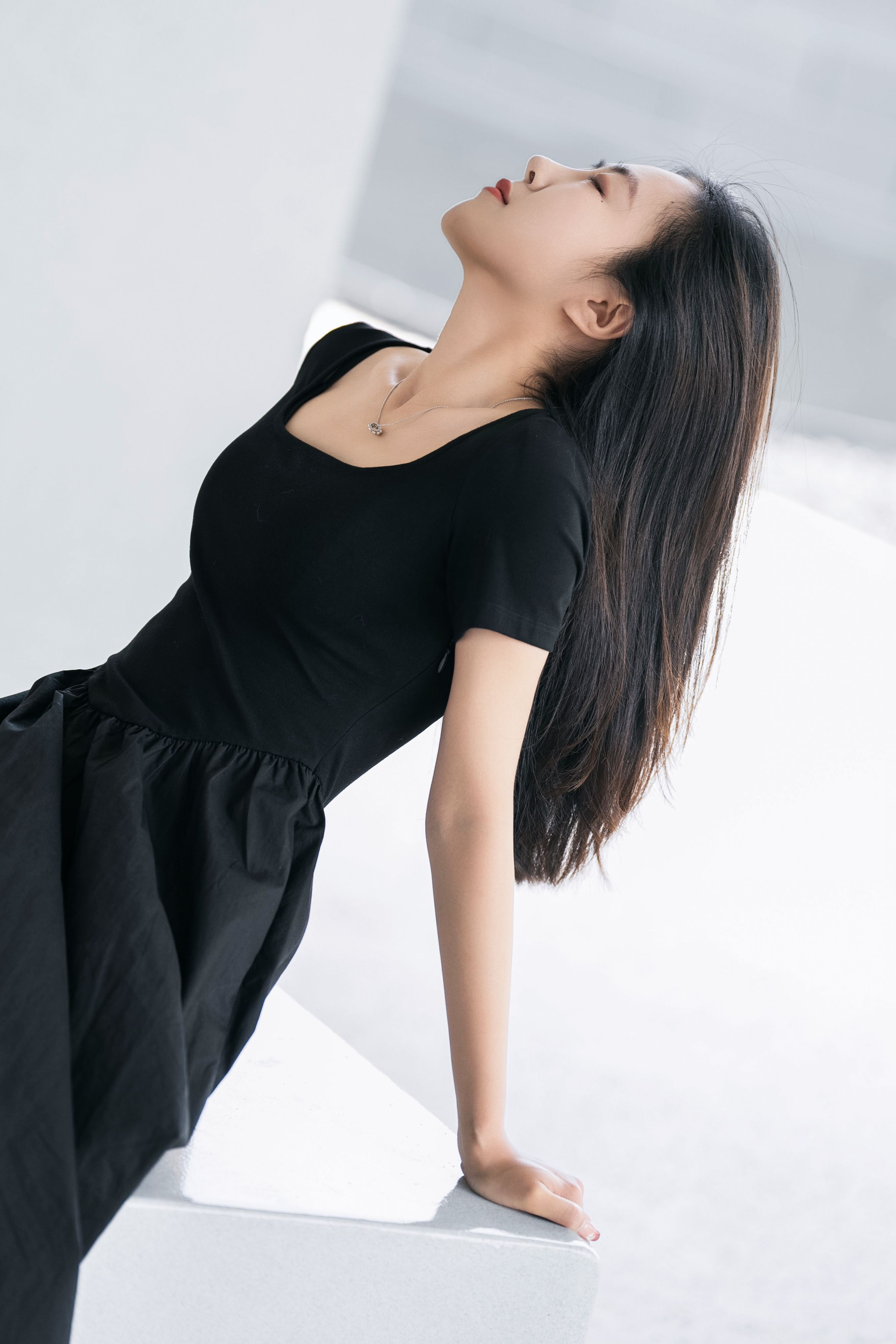 Fashionable woman in a black dress posing elegantly indoors, creating a serene and stylish portrait.