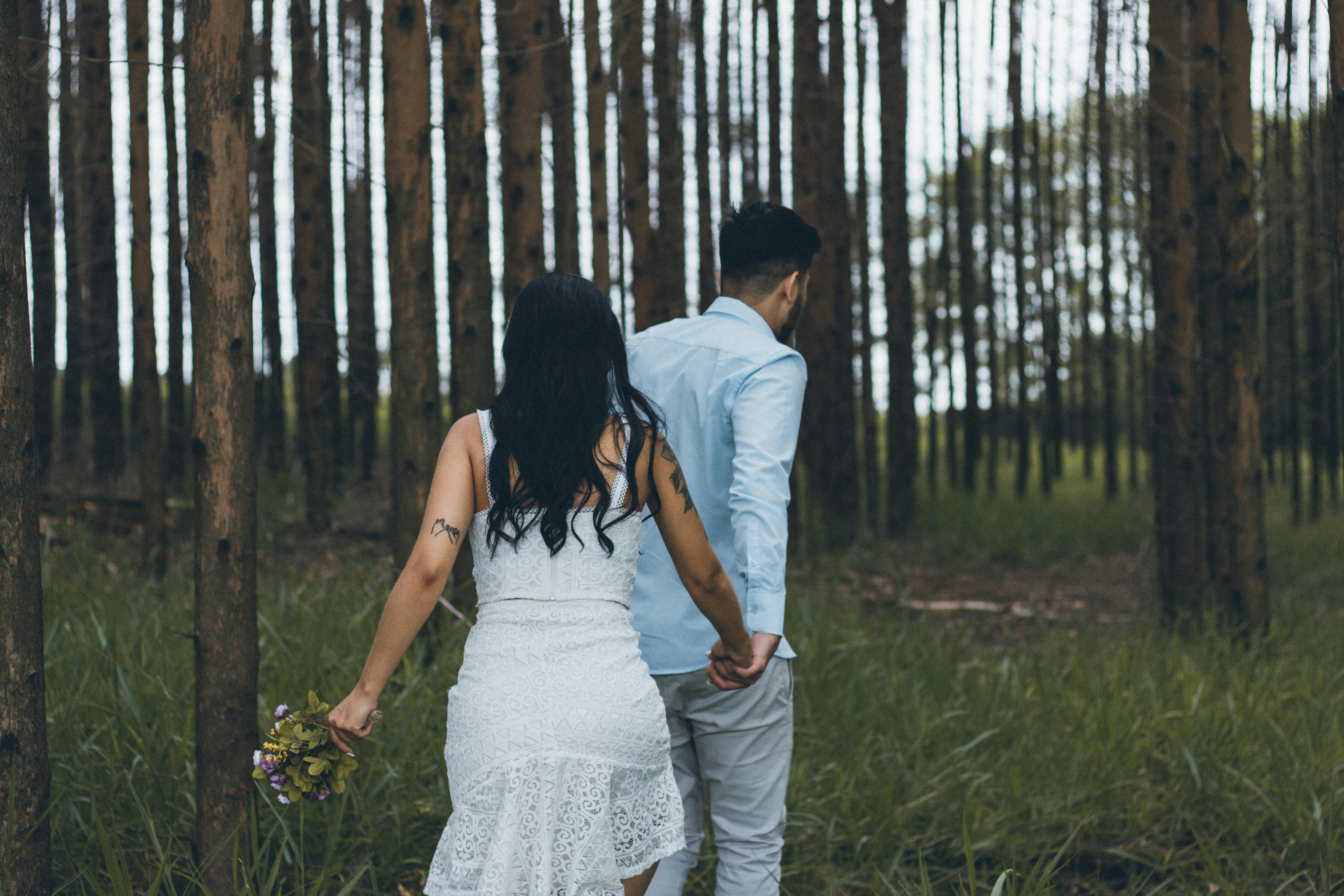 A couple holding hands, walking together in a serene forest setting.