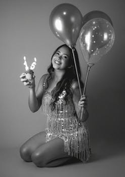 A young woman celebrates her 15th birthday with balloons and a cupcake in black and white.