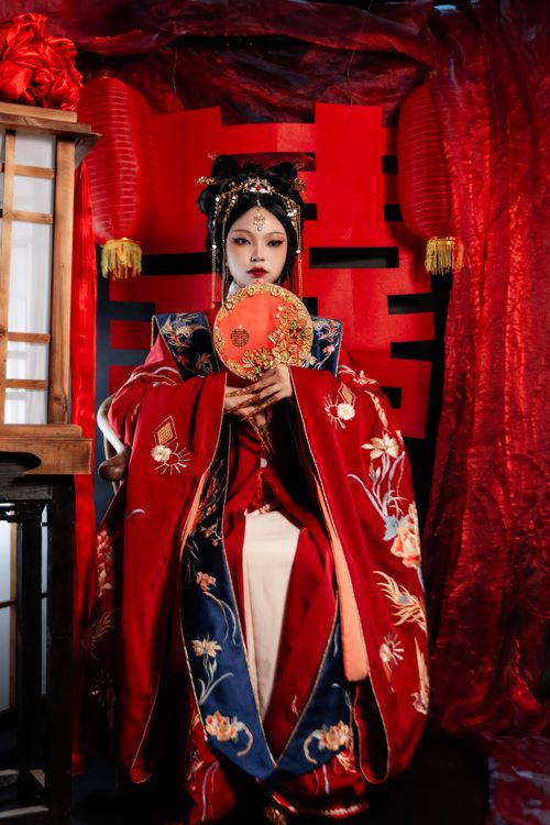 Free Portrait of a woman in ornate traditional red clothing with decorative fan indoors. Stock Photo