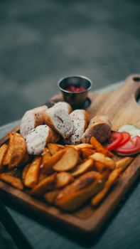 A delectable platter featuring sliced meat, potato wedges, and vegetables served on a wooden tray.