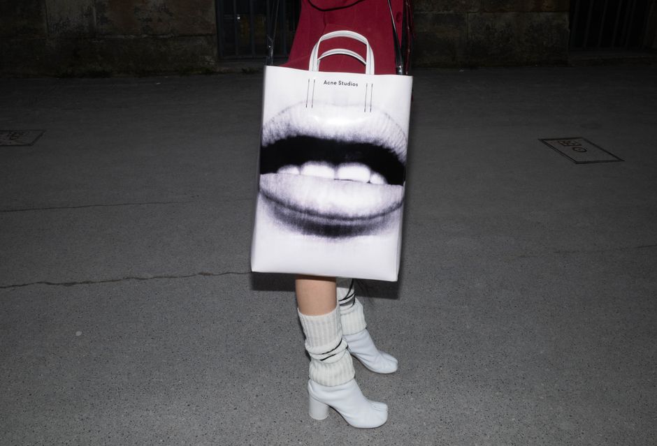 Close-up of a stylish bag with art print, paired with high heels on a nighttime pavement.