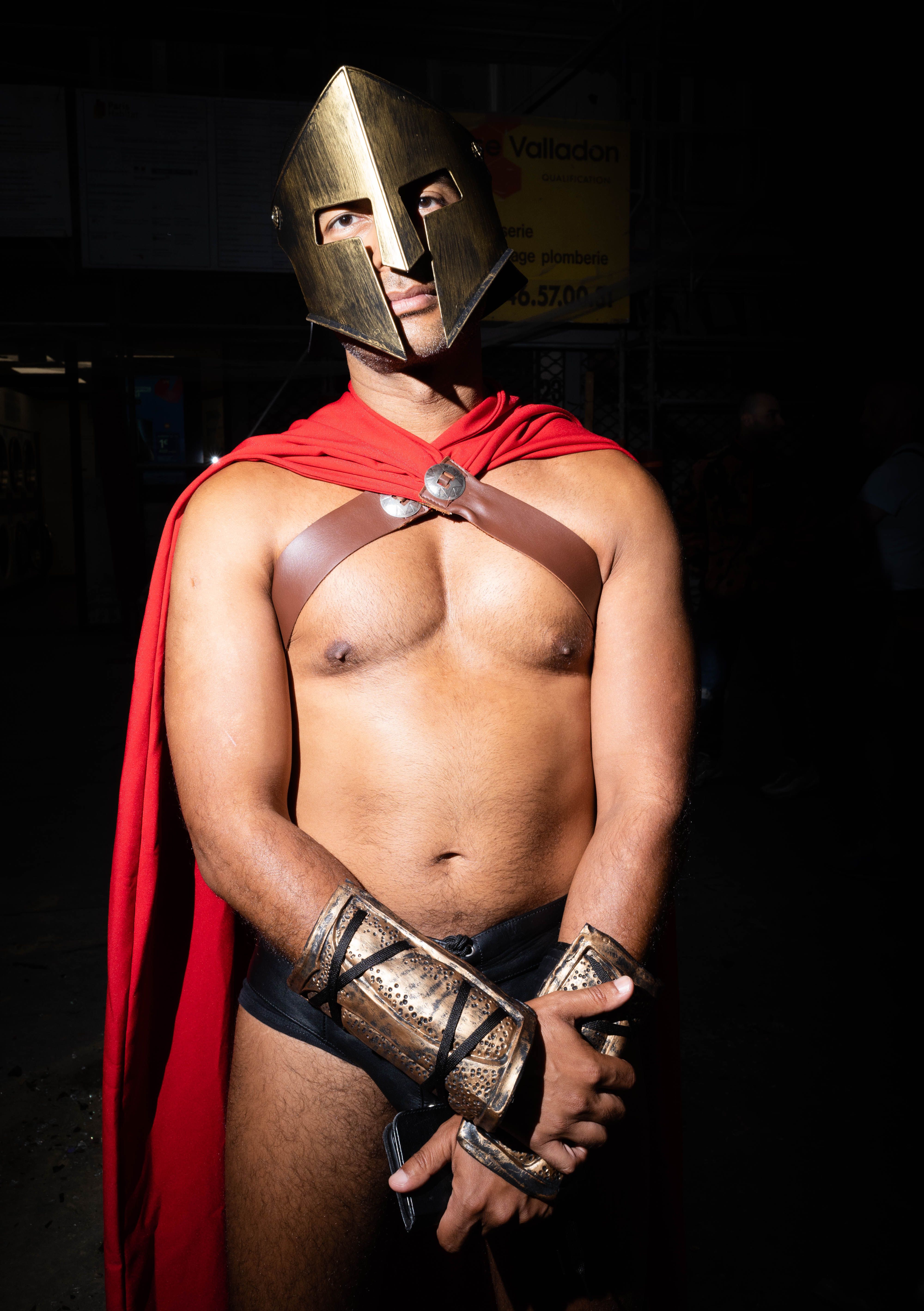 Man wearing a Spartan costume with helmet, cape, and arm guards on a dark background.