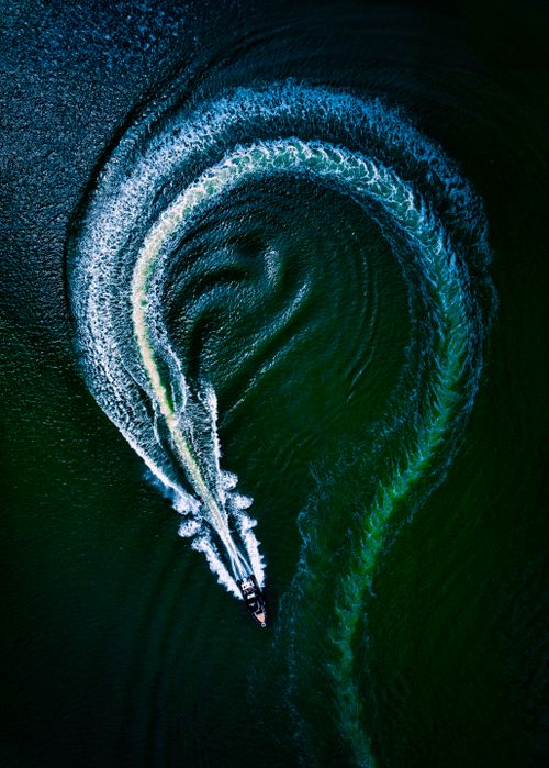 Free Aerial view of a speedboat creating a swirling wake pattern on a dark green sea. Stock Photo