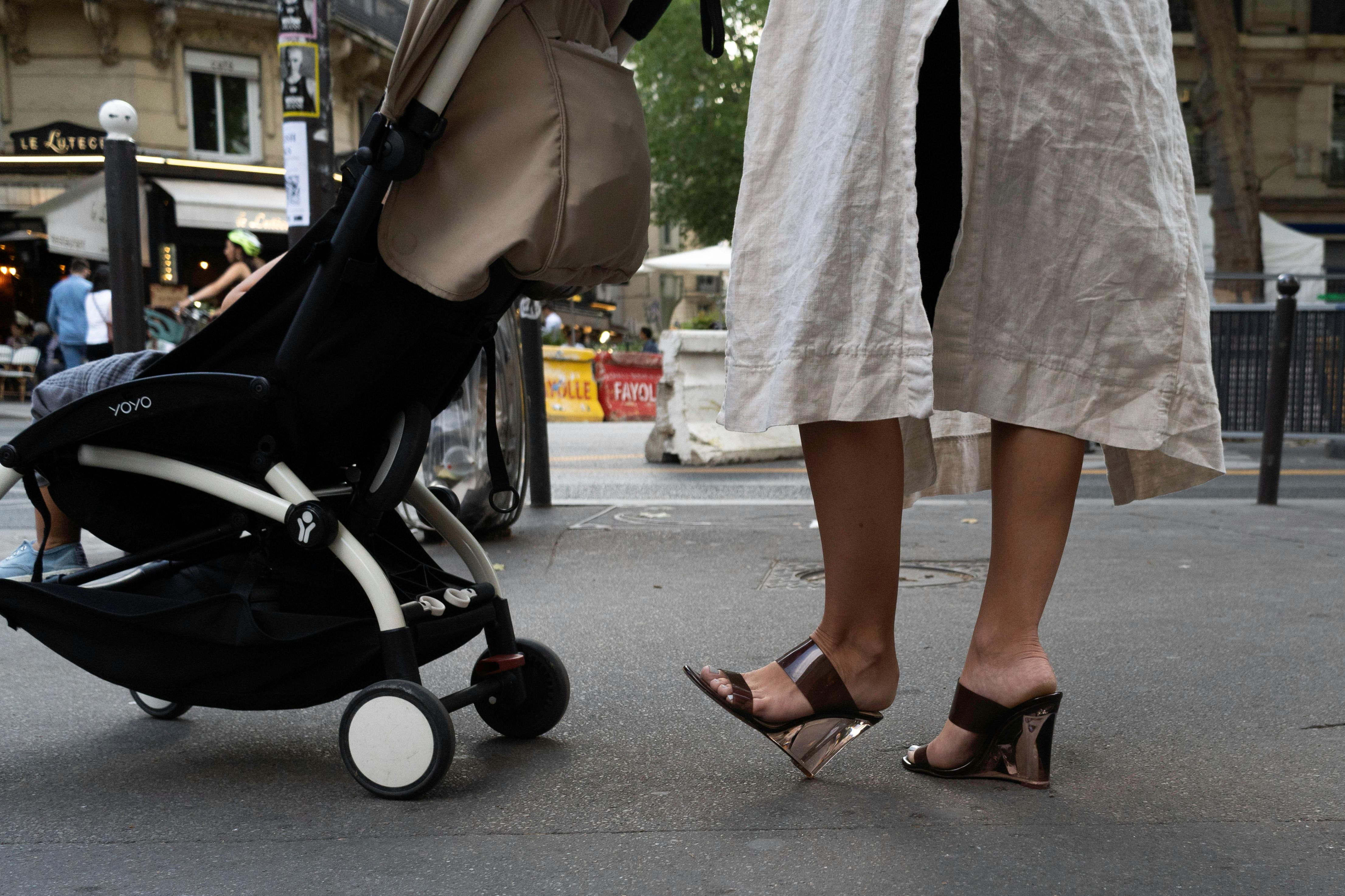 Stylish woman pushing a stroller in urban street setting, showcasing fashion and city life.