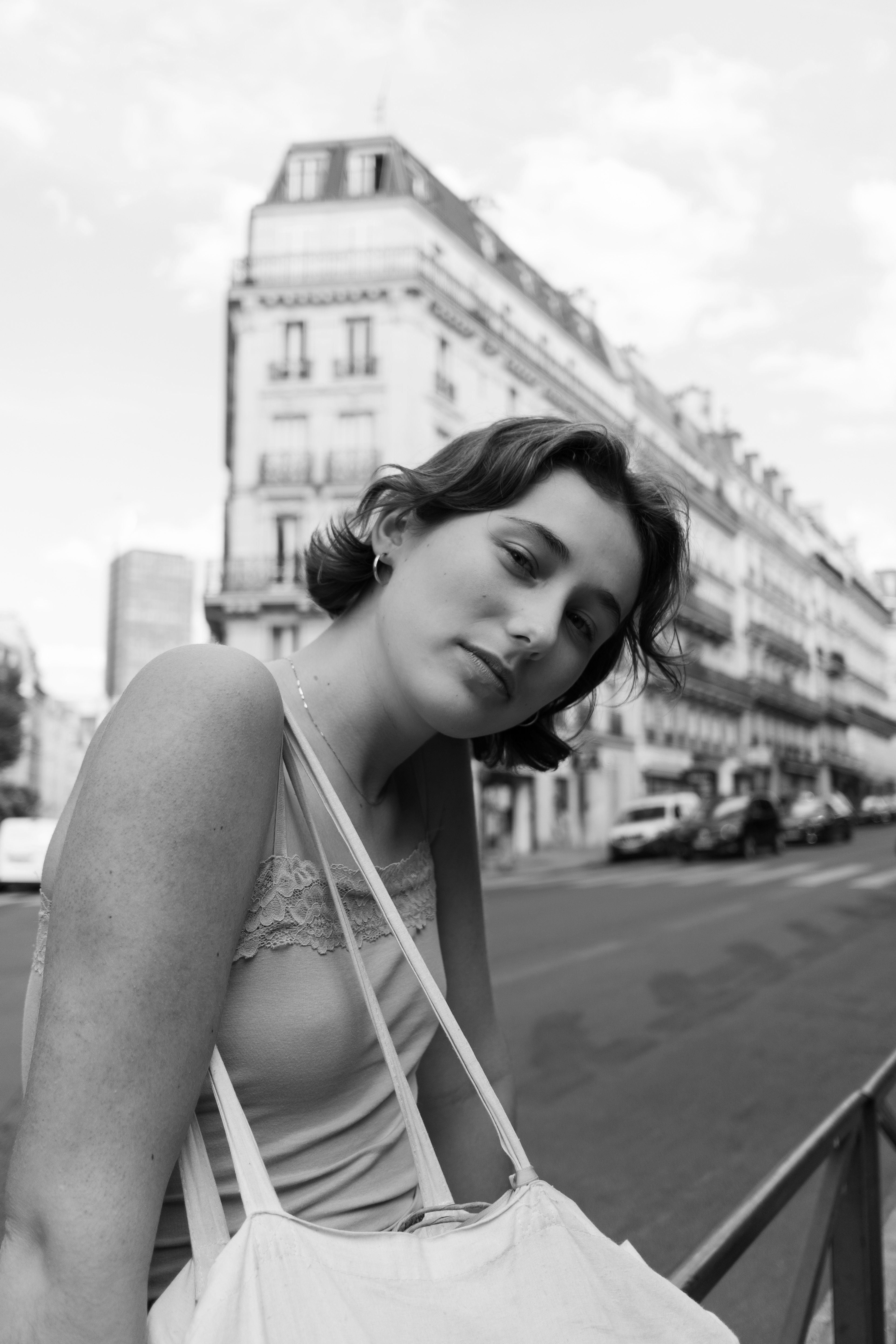 Black and white portrait of a woman posing on a city street with a classic architectural backdrop.