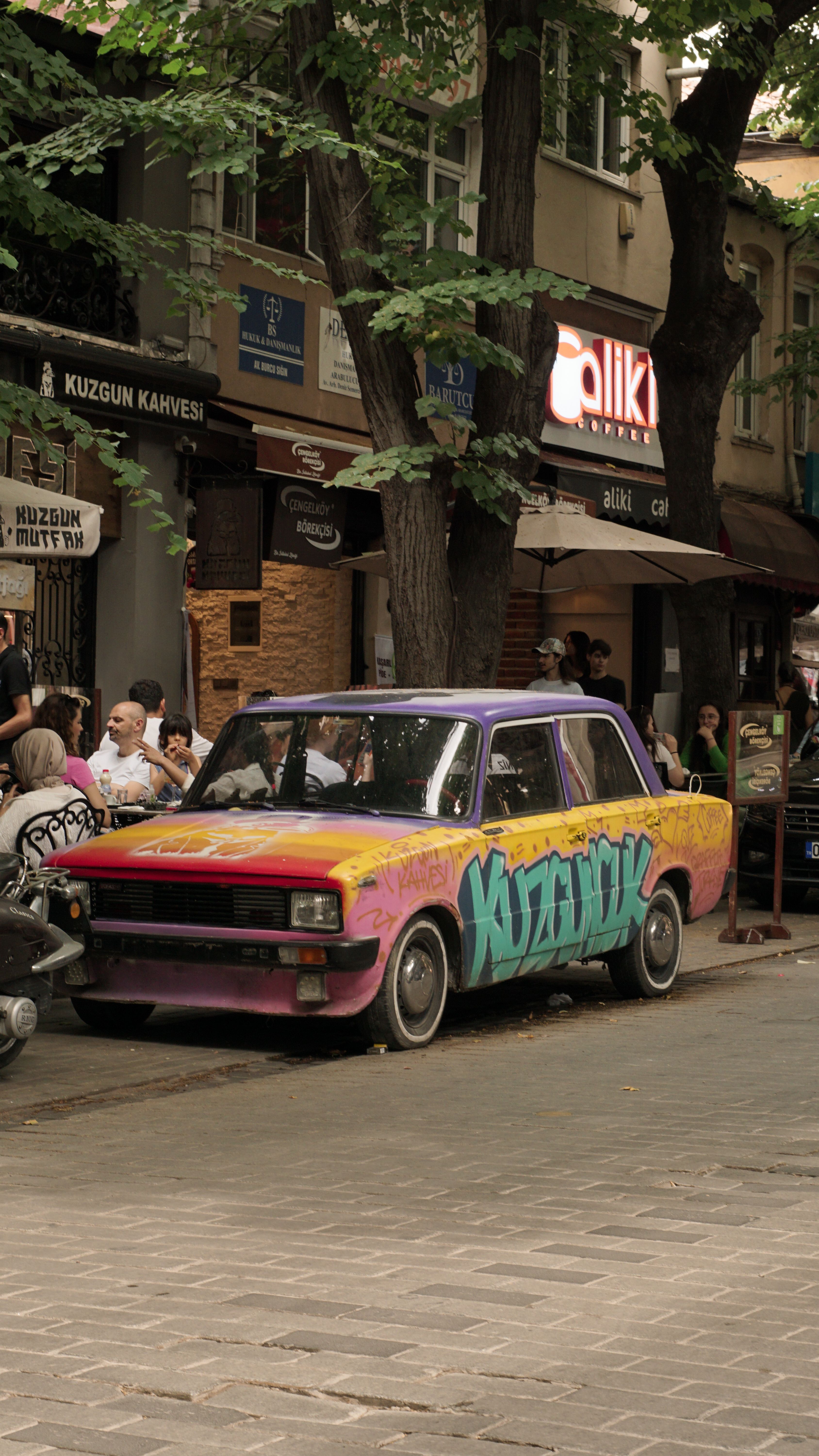 A vibrant retro car with graffiti parked on a bustling Istanbul street.