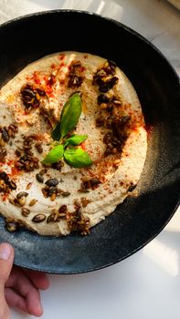 Delicious hummus garnished with seeds, spices, and fresh basil leaves in sunlight.