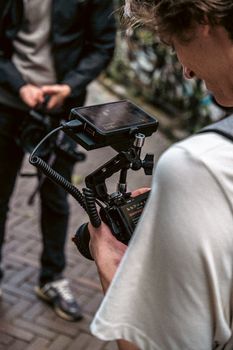 Close-up of a videographer holding a camera rig with a monitor, focused on a device outdoors.