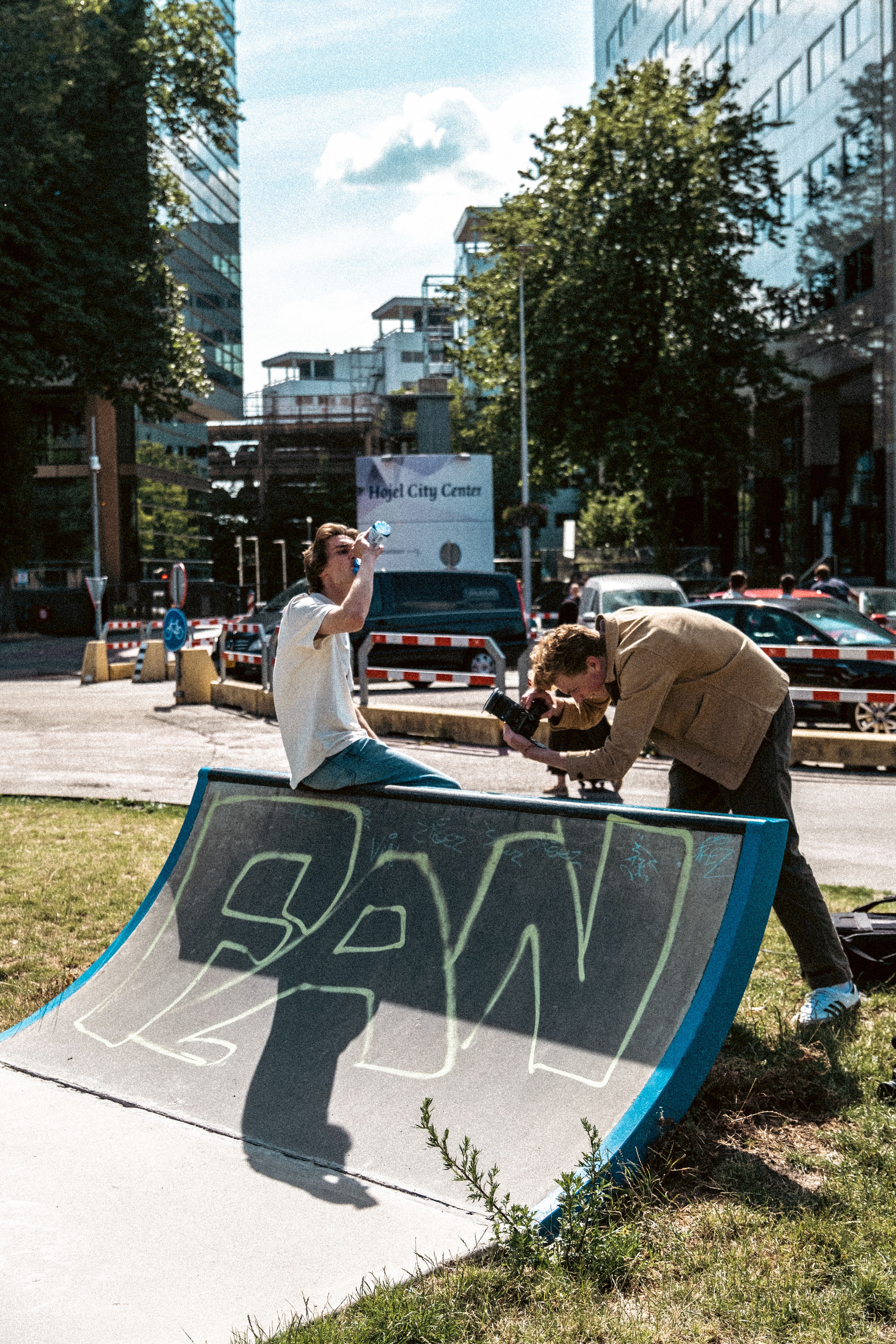 Photographer capturing a model at an urban skatepark with city backdrop.