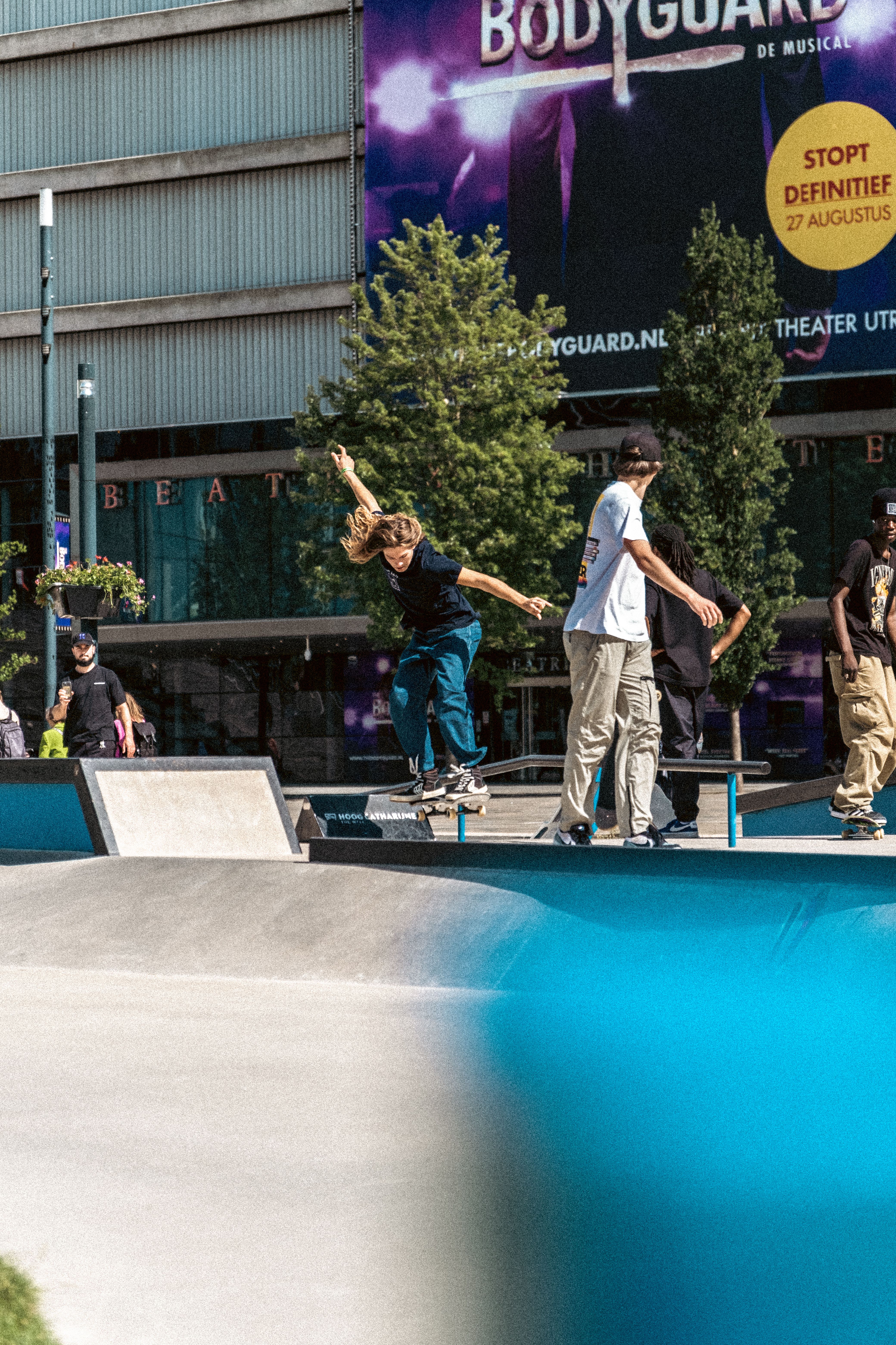 Skateboarders showcasing their skills at an urban skatepark under bright daylight.